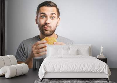 Young man holding a piece of hamburger. Student eats fast food. Burger is not helpful food. Very hungry guy. Diet concept. Wall mural