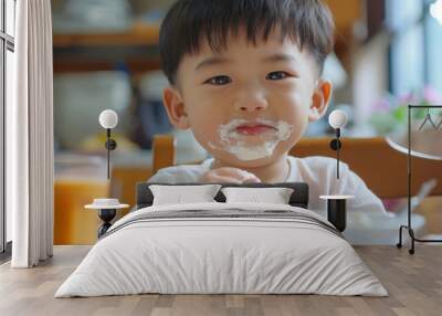 A child joyfully eats at the table, leaving a yogurt mess on his face during breakfast Wall mural