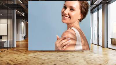 A beautiful tender woman put a natural cosmetic scrub to her shoulder and smiles Wall mural