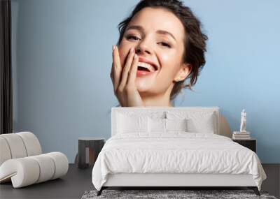 Beautiful model covering joyfully smiling open mouth with hand. Positive playful mood Wall mural