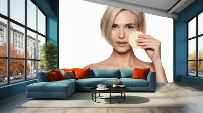 Beautiful woman applying sponge for face cleaning looking at camera. Facial skin cleansing, peeling and scrubbing cosmetic product. Wall mural