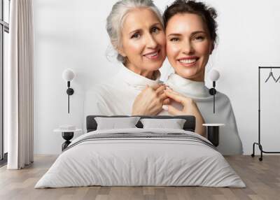 Cosmetic portrait of two women of different ages and generations smiling and holding hands on a white background. A young beautiful woman and her mother looking happily into the frame together Wall mural