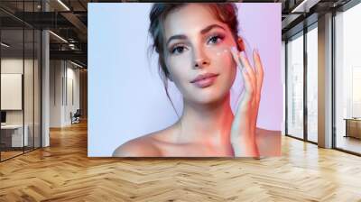 Cute woman with natural make-up applying moisturizing facial cream. Portrait of wonderful female looking at camera with calmness. Beauty and skincare concept Wall mural