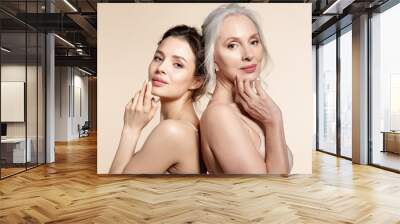 Elderly and young women with smooth skin and natural makeup standing back-to-back.  Wall mural