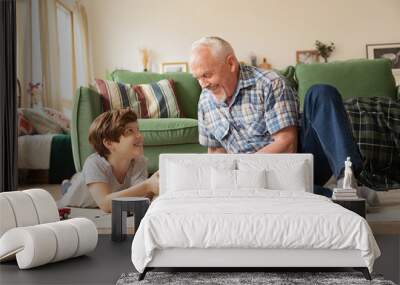 Elderly smiling grandfather giving little funny grandson present on holiday on warm floor among toys Wall mural