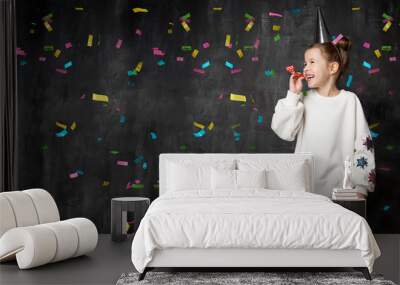 Little girl laughs and has fun at a celebration on the background of a school board and confetti with a free place on the left Wall mural