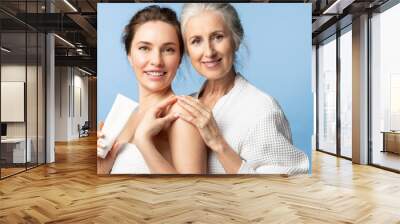 Mother and daughter holding skin cream and smiling. Two beautiful women of different ages and generations together on a blue background. Wall mural