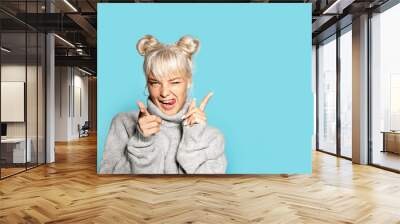 Portrait of beautiful blonde girl wearing cozy grey sweater and making faces. Pretty model in cheerful mood posing on blue background. Copy space in right side. Winter and emotion concept Wall mural