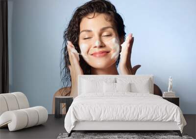 Smiling young woman washing foam face by natural foamy gel. Satisfied girl with bare shoulders applying cleansing beauty product on cheeks closed eyes. Personal hygiene, skincare daily routine. Wall mural