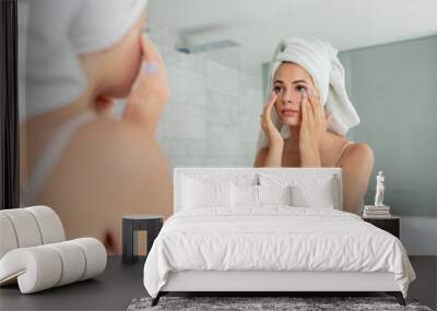 Young woman applying anti-wrinkle eye cream standing behind mirror in home bathroom. Beautiful girl wearing bath towel on head portrait. Cosmetology and beauty procedure. Skin care after cleansing Wall mural