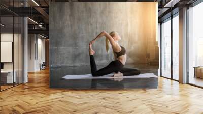 Young woman doing ashtanga yoga practice in a loft studio, surrounded by bright sunlight. Beutiful girl meditating makes herself a healthy body and strengthening the spirit. Wall mural