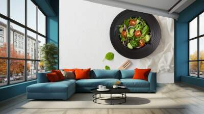 Fresh healthy vegetarian vegetables salad with lettuce and tomatoes, red onion and spinach in black bowl on white background with spatula fork and white kitchen cloth. Wall mural