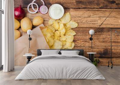 Fresh organic homemade potato crisps chips with sour cream and red onions and spices in paper bag on wooden background. With fresh yellow potatoes Wall mural