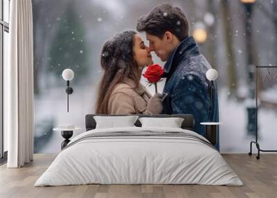 In love couple kissing in snow at city street. Handsome man and beautiful young woman with red roses, outdoors portrait. Happy Valentine's day. Wall mural