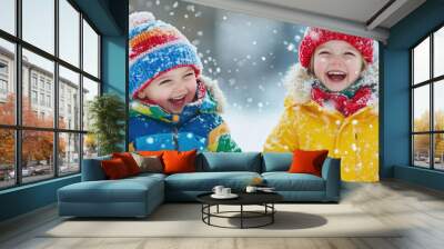 Two children dressed in colorful winter clothes are laughing and playing in the snow during a joyful winter day. Wall mural