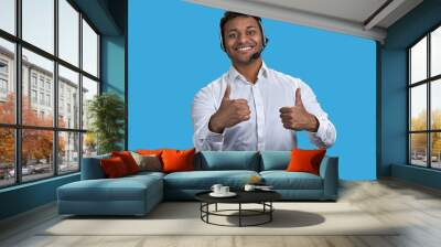 Portrait of indian businessman wearing headset showing two thumbs up. Isolated on blue. Wall mural