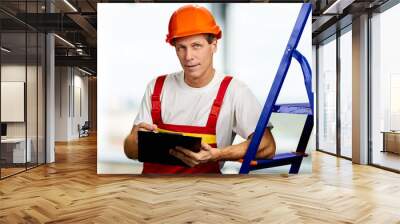 Portrait of mature foreman with clipboard. Middle-aged contractor with hardhat and clipboard looking on new object. Wall mural