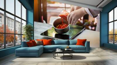 Red liquid pours into saucepan. Hand in glove holds jug. Fresh tomato juice. Restaurant chef makes tasty sauce. Wall mural