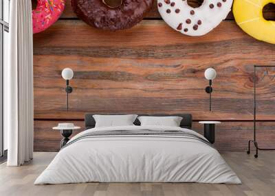 Row of different donuts on brown wooden background. Set of multicolored sweets. Space for text. Wall mural