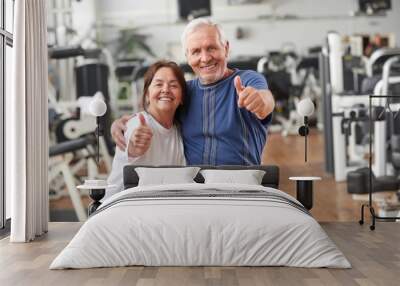 Senior couple giving thumbs up at gym. Happy couple of seniors gesturing thumbs up at fitness center. People and healthy lifestyle concept. Wall mural