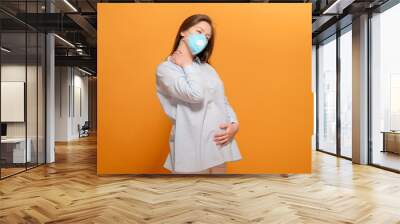 coronavirus pandemic, young pregnant woman on yellow background in protective medical mask, pain in the neck Wall mural