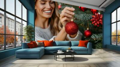 A woman decorates a Christmas tree with red ornaments while enjoying the festive atmosphere of the holiday season Wall mural