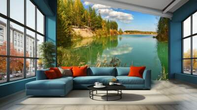 Turquoise lake with muddy water and colorful autumn forest on the shore, under a blue sky with white clouds Wall mural