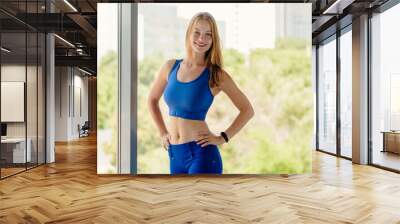 Portrait of beautiful smiling slim sporty female athlete in blue sportswear Wall mural