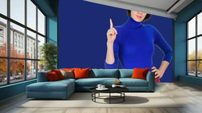 Successful young brunette woman pointing up on navy color background Wall mural