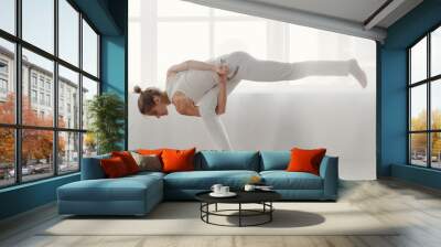 Young attractive woman in white sportswear demonstrating yoga position, body balance on one leg Wall mural