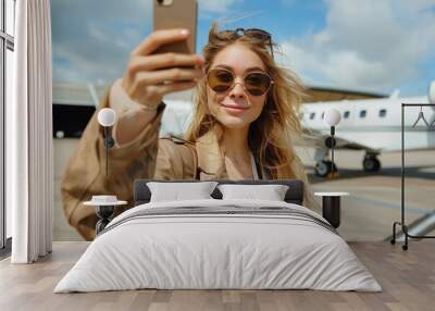 A stylish young woman with sunglasses takes a selfie with a luxurious private jet in the background at an airfield Wall mural