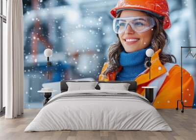 A female worker in winter gear smiles while using a tablet on a snowy construction site, showcasing safety and technology. Wall mural