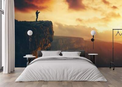 A man stands on a cliff edge, taking in the breathtaking view of the valley at sunset. Wall mural