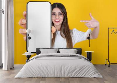 Cool application recommending. Excited smiling caucasian woman demonstrating big smartphone with empty blank screen mockup. Selective focus on mobile phone blurred lady pointing white display. Wall mural