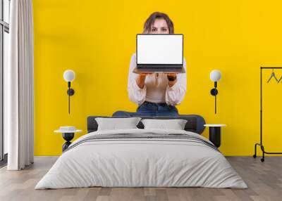 Demonstrating laptop mock up,  full body portrait of young caucasian woman sit floor demonstrating laptop mock up. Young girl showing empty screen pc computer holding it in front of her face. Wall mural