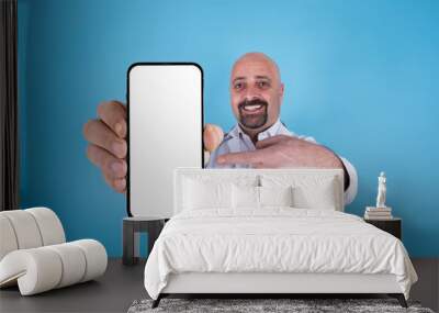 Doctor recommendation concept idea image. Portrait of excited doctor holding big smartphone pointing white blank screen for mock up. Looking camera. Blue background and copy space. Bald bearded man. Wall mural