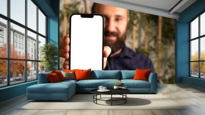 Showing modern smartphone, portrait of caucasian bearded man showing modern smartphone. Selective focus on hand. Mobile phone mock up with white blank screen. Application recommend concept photo idea. Wall mural