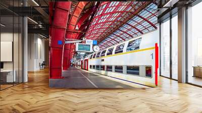 Antwerp, Belgium. Central indoor railway station. Platform made of red metal constructions with clock and panel with departure or arrival schedule. Modern double decker high-speed train Wall mural