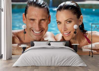 Close up portrait of a beautiful happy man and woman couple resting on their hands at the side of a sun bathed swimming pool smiling with perfect teeth. Wall mural