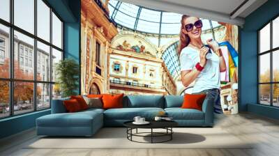 Discover most unexpected trends in Milan. Full length portrait of smiling fashion woman in eyeglasses with colorful shopping bags and coffee cup in Galleria Vittorio Emanuele II Wall mural