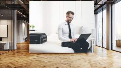 Young businessman on bed working with a laptop from his hotel room Wall mural