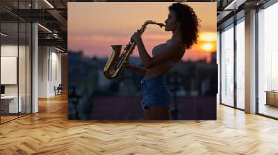 Young curly girl with sax on the roof at sunset Wall mural