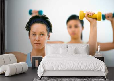 Young women at gym lifting hand weights. Wall mural