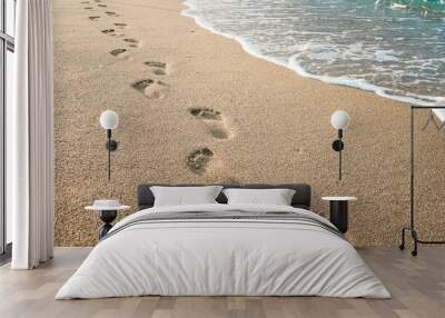 Footprints of human feet on the sand near the water on the beach Wall mural