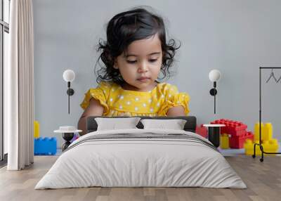 Adorable young desi girl using brightly colored building blocks against a white background Wall mural