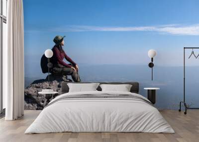 A traveler sits on a rock on a high mountain with a beautiful view of the sky. Wall mural