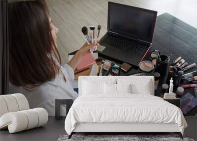 Girl make-up artist shows a set of makeup brushes, focus on laptop screen Wall mural