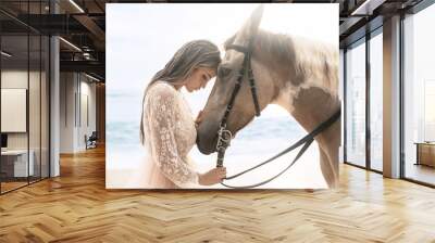 Happy fashionable young woman in a white dress posing with a horse on the beach. Wall mural