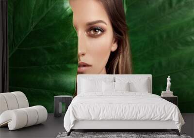 Luxury Portrait of a Beautiful young woman with natural makeup holds a big green leaf on a blurred green background. Spa and wellness. Youth, teens and skin care concept. Close up Wall mural