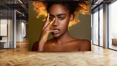 Portrait of a sensual african woman with gold paint on her face and hands. She bit her fingers. Ethnic fashion and style. Wall mural